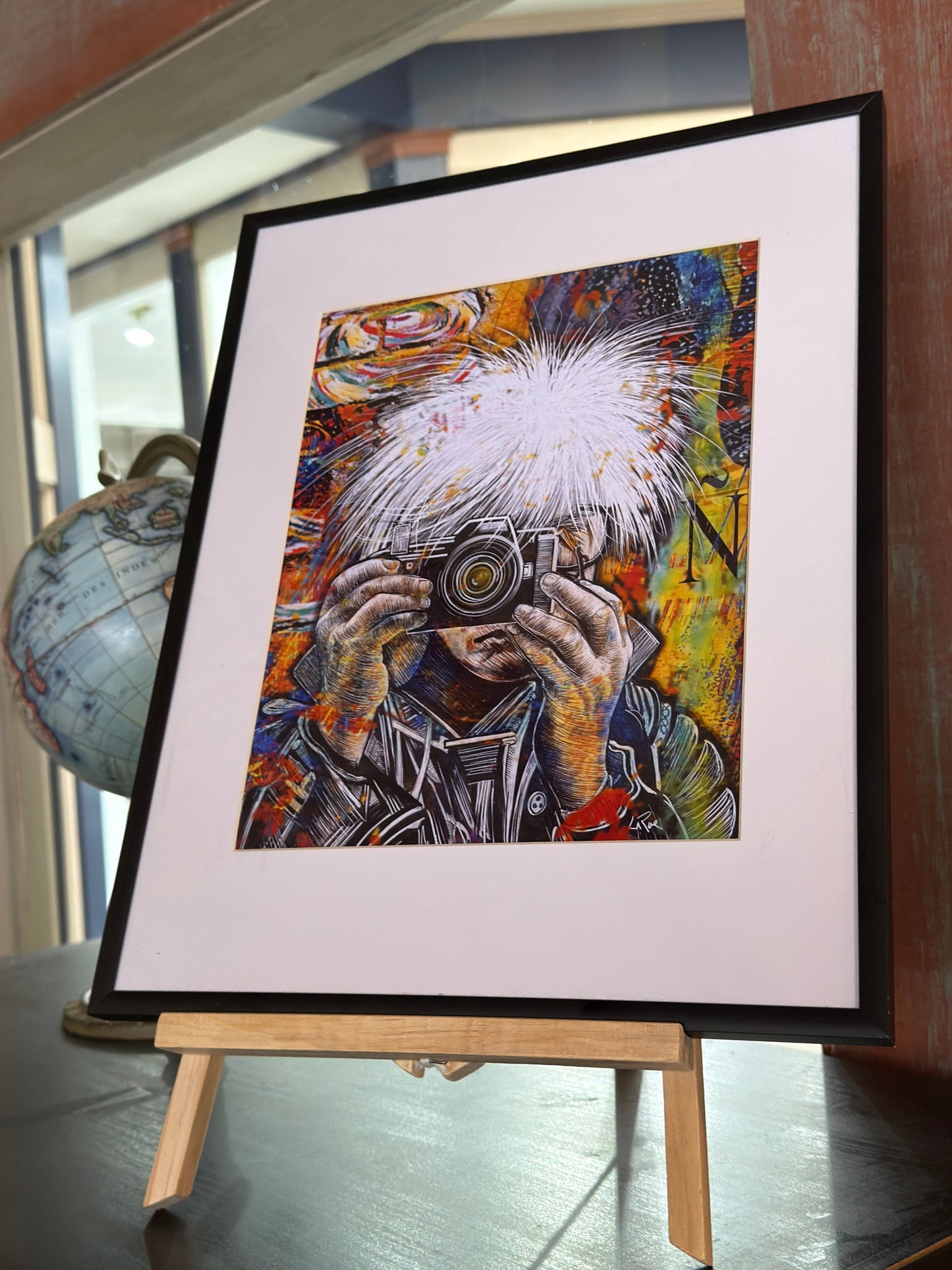 Framed artwork of Andy Warhol holding a camera with a colorful abstract background.