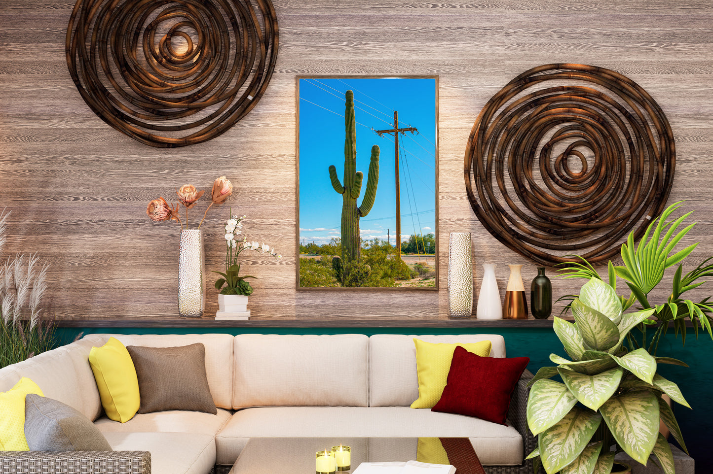A framed vertical canvas print of a saguaro cactus in a desert landscape, displayed on a wood-paneled wall above a modern sectional sofa in a styled living room.