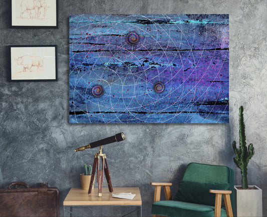 A square abstract wall art print featuring a blue and purple cosmic design with white geometric lines and circular motifs, displayed on a textured gray wall in a styled room setting with a green chair, side table, and cactus. Blue Trinity by Doug LaRue