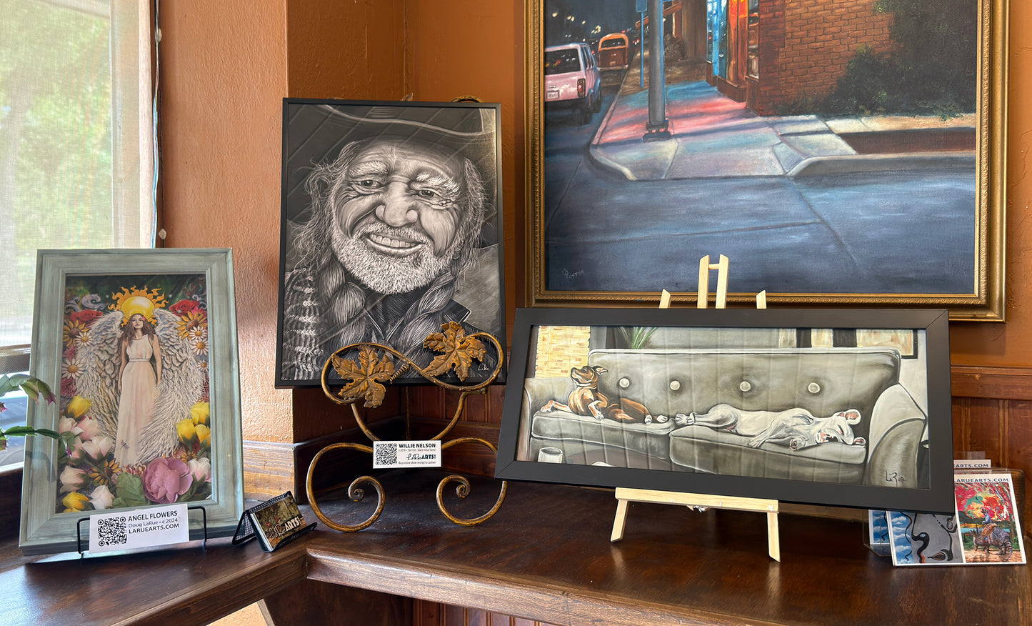 Collection of framed artworks on a wooden surface with a window in the background.