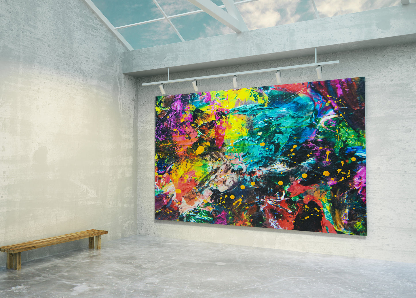 A large rectangular abstract canvas print with vivid splashes of blue, green, yellow, pink, purple, red, and orange displayed on a gallery wall in a modern concrete room with a wooden bench and skylight.
