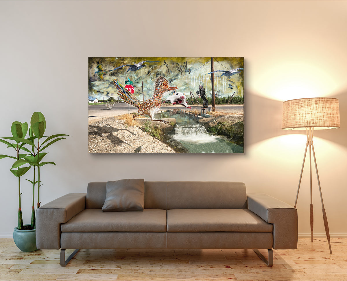 A surreal collage-style artwork showing a large brown and white bird in the foreground, a white mouse mid-leap beside a small stream, a stop sign, utility poles, a mural with flying birds, and a person riding a unicycle in the background. LaRue Road by Doug LaRue displayed on a beige wall above a modern brown sofa in a styled living room with a floor lamp and potted plant.