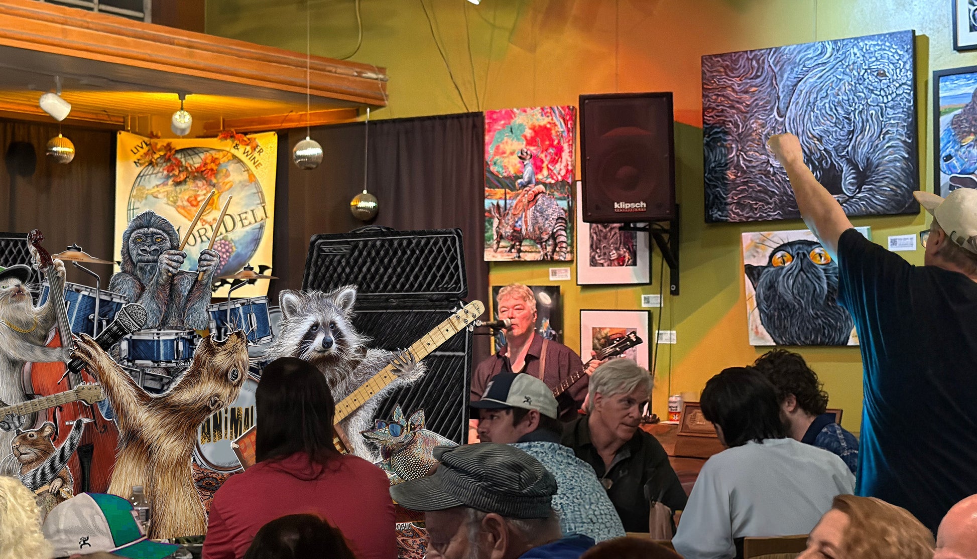 Art gallery with colorful paintings on a wall, people watching The Animals band with Armadillo Cowboy Sunset by Doug LaRuemixed media canvas on the wall next to the stage.