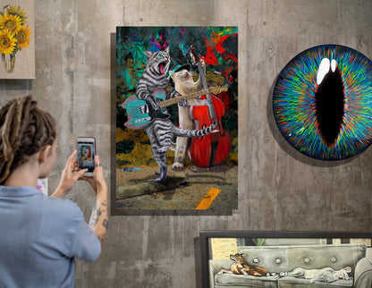 A person takes a photo of a colorful canvas print hanging on a gray concrete wall. The artwork depicts two cats playing string instruments together in a vibrant, multicolored scene.