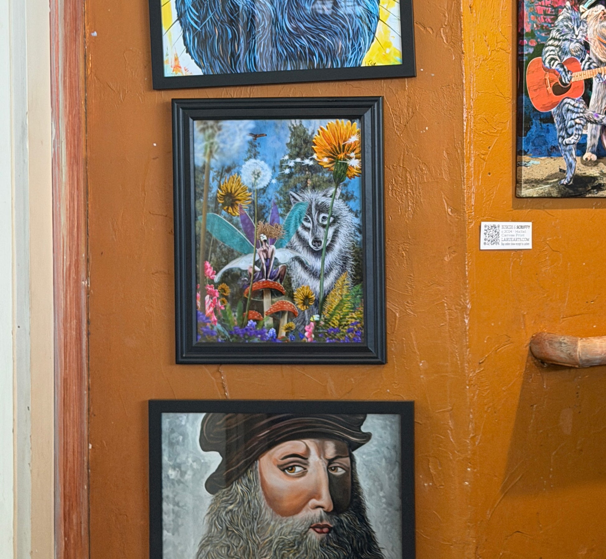 Framed artworks on an orange wall. Fairy Security by Doug LaRue