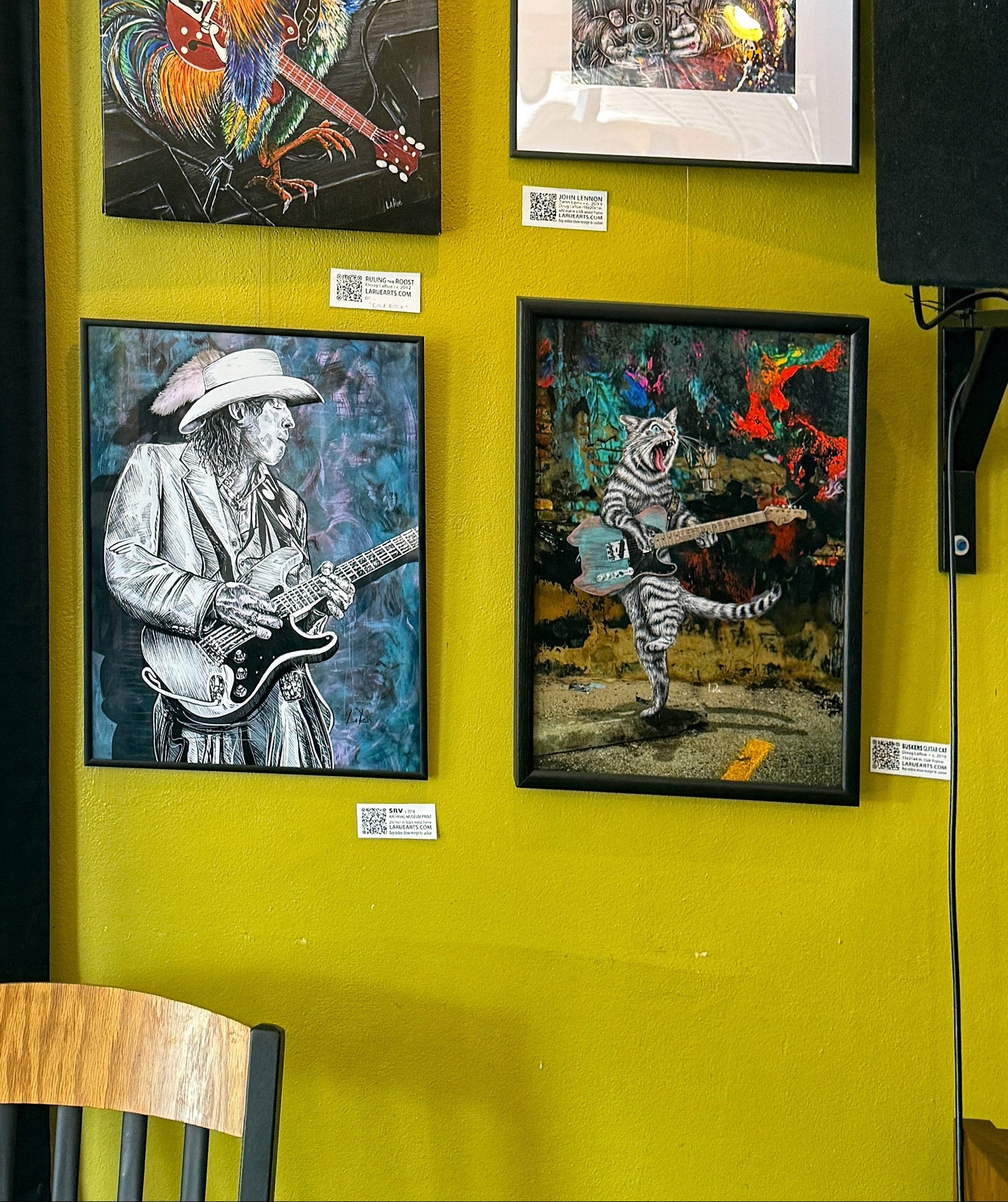 Four framed artworks on a yellow wall, featuring musicians and animals.