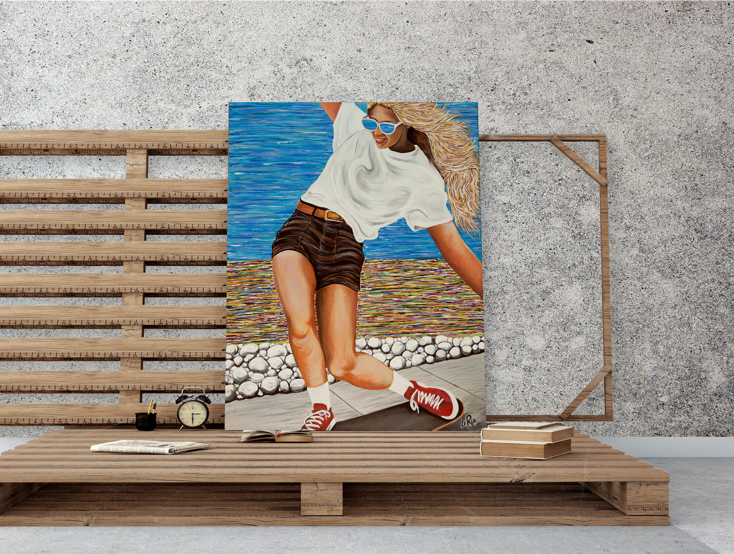 Framed artwork of a person in sunglasses and shorts on a wooden shelf against a textured wall. Woman skateboarding  a colorful abstract oceanside beach path by a colorful beach scene Girls Like You is an acrylic painting by Doug LaRue