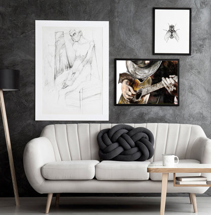 Three framed artworks on a textured grey wall over a modern white couch. SRV Sketch b y Doug LaRue