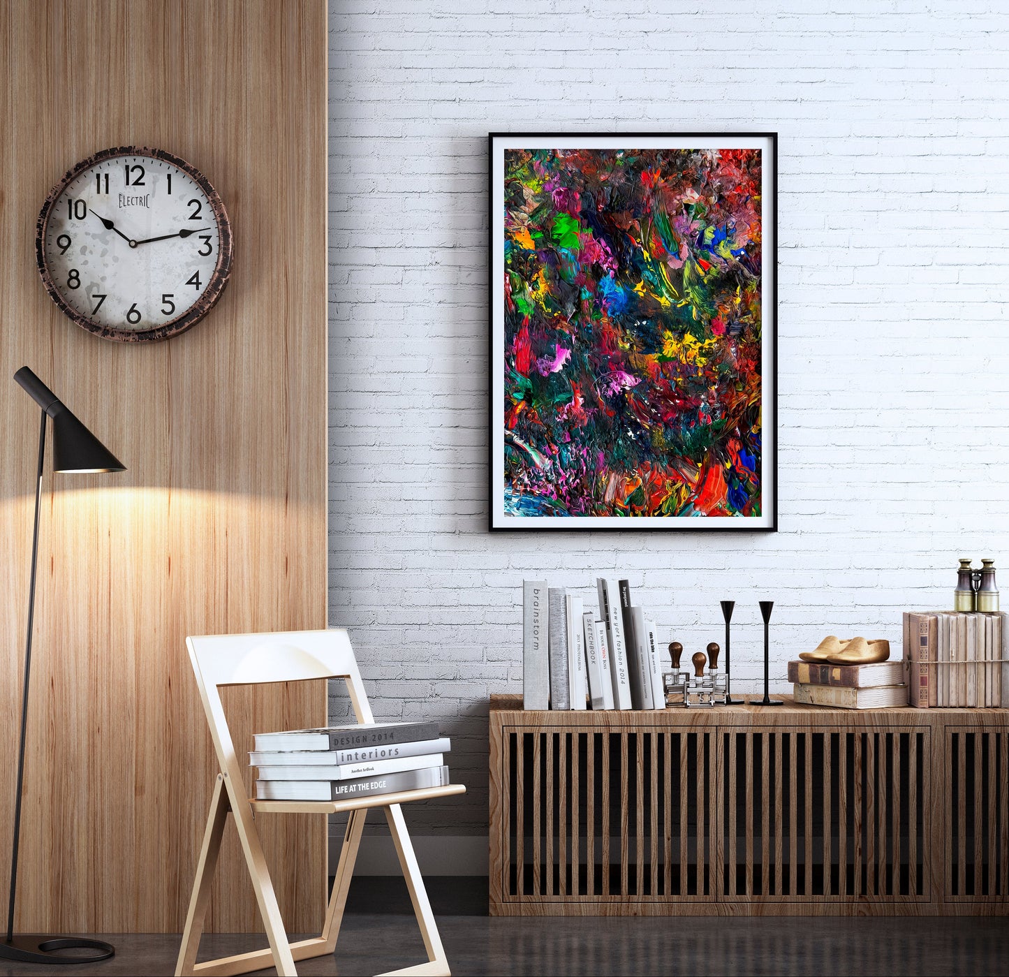 A colorful abstract canvas art print in a black frame hangs on a white brick wall in a modern, stylishly decorated room with a wooden credenza, books, a folding chair, and a wall clock. V19 Brentwood by Doug LaRue