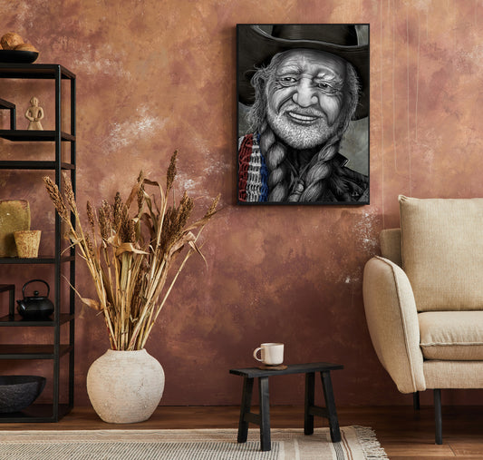 A framed black and white portrait print of a cowboy hanging on a textured terracotta wall in a styled living room setting with a beige armchair, a small table, and a vase of dried grass.  Willie Nelson by Doug LaRue